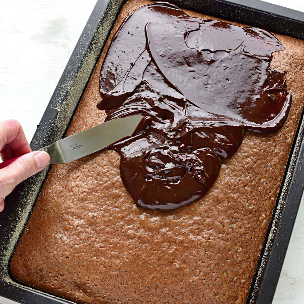 Spreading chocolate glaze over buttermilk sheet cake.